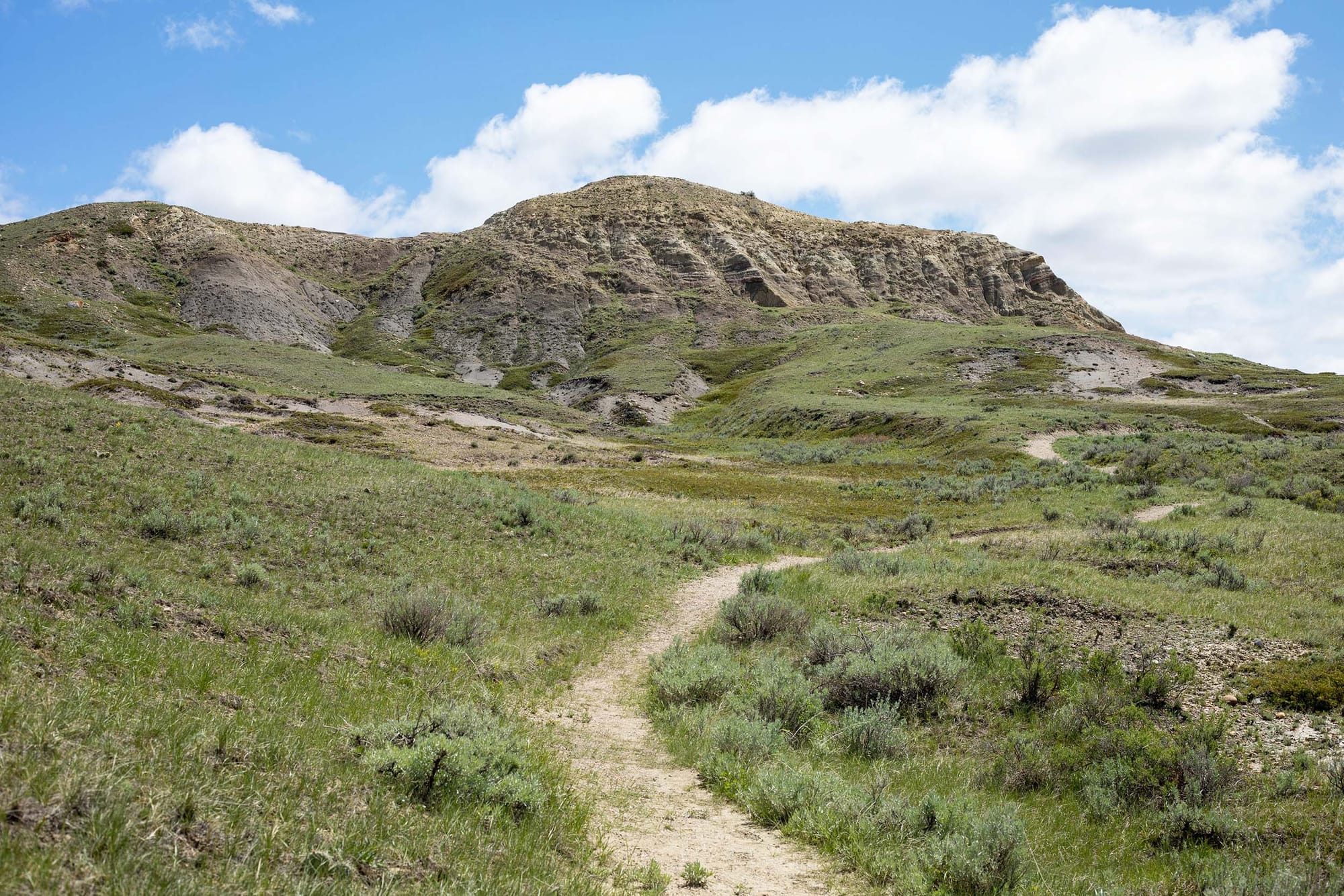 A path leads through grassland up toward a rocky hill