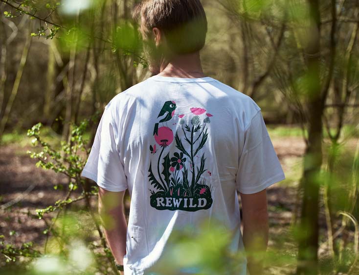 Back view of a person wearing a white T-shirt with the word "Rewild"