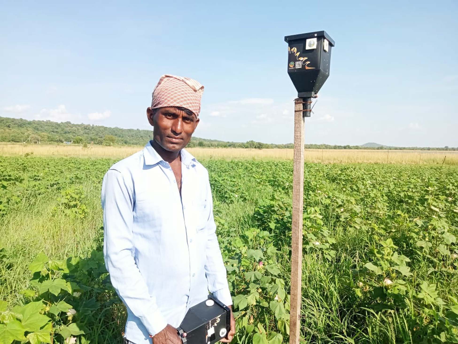 A person stands in front of an agricultural field next to a black lighting box mounted on a stake