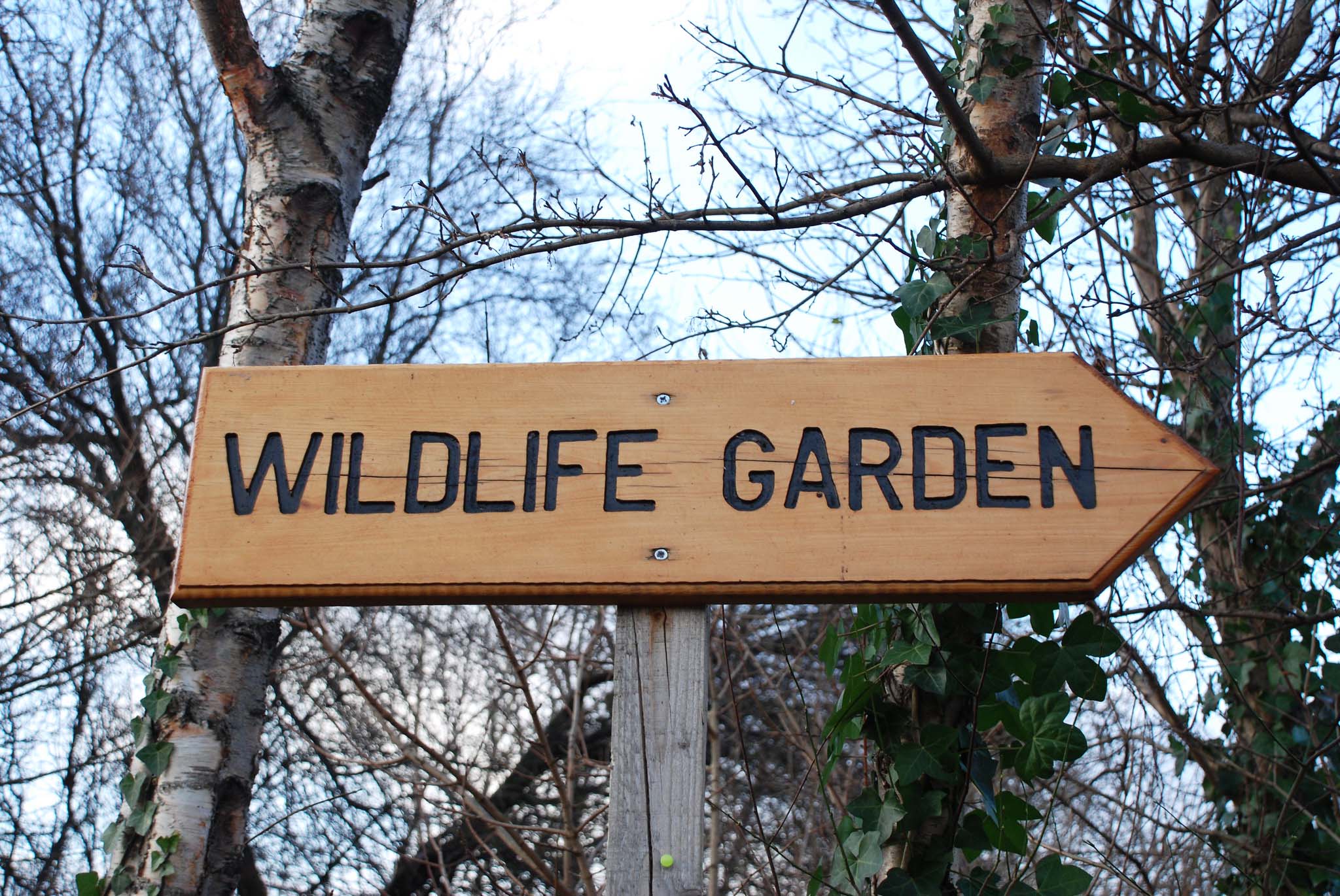 In a natural environment, a wooden sign reads "wildlife garden"