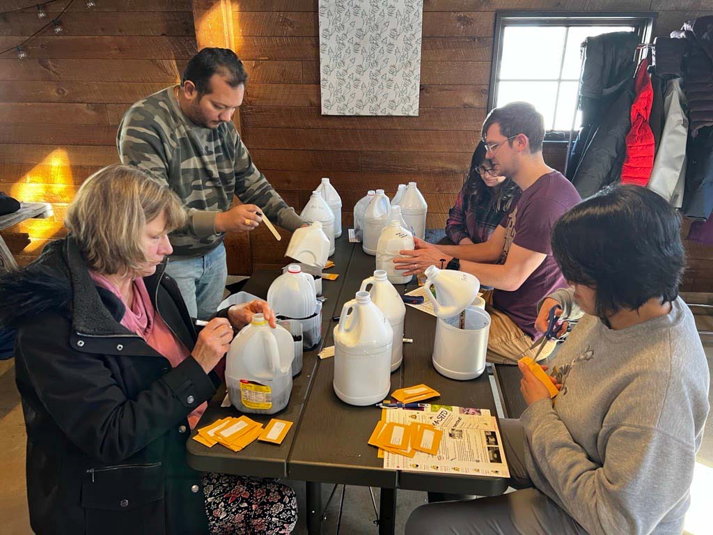 A group of people sitting indoors around a table planting seeds into plastic jugs