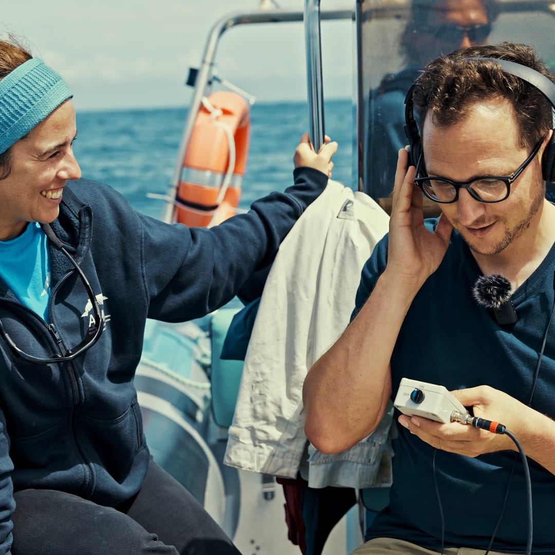 Two people on a boat. One is listening to audio through headphones