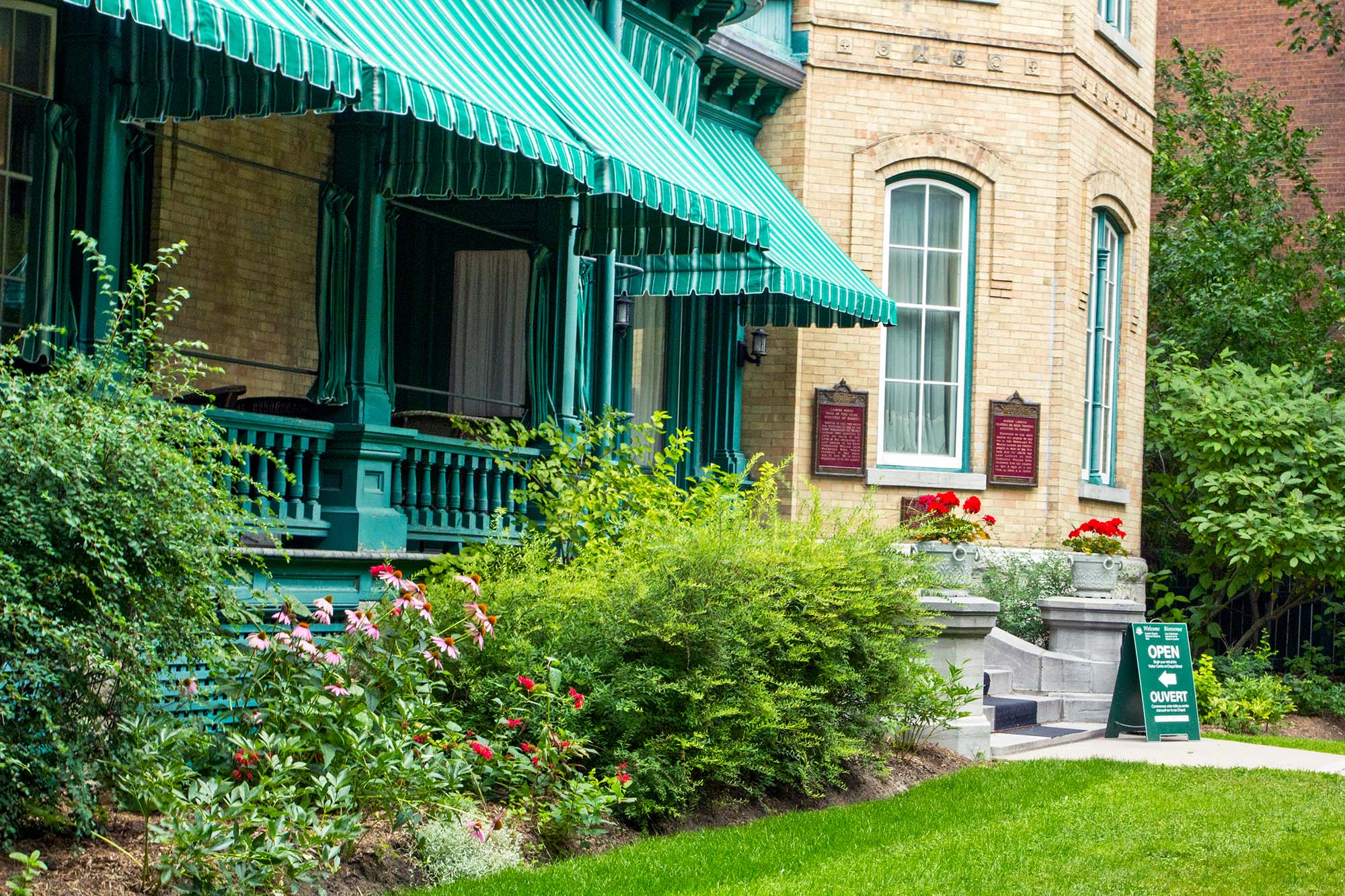 Between a heritage house and a green lawn, a flowerbed contains a variety of plants