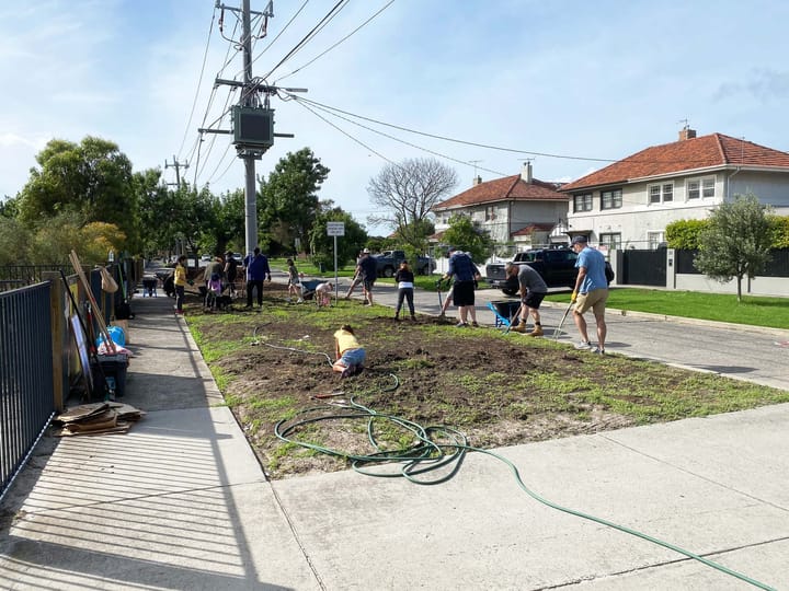 A group of people tending some land between road and sidewalk in a residential neighbourhood