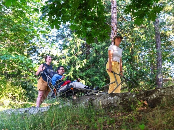 A group of people in a forested area, smiling. One is using a specially modified wheelchair.