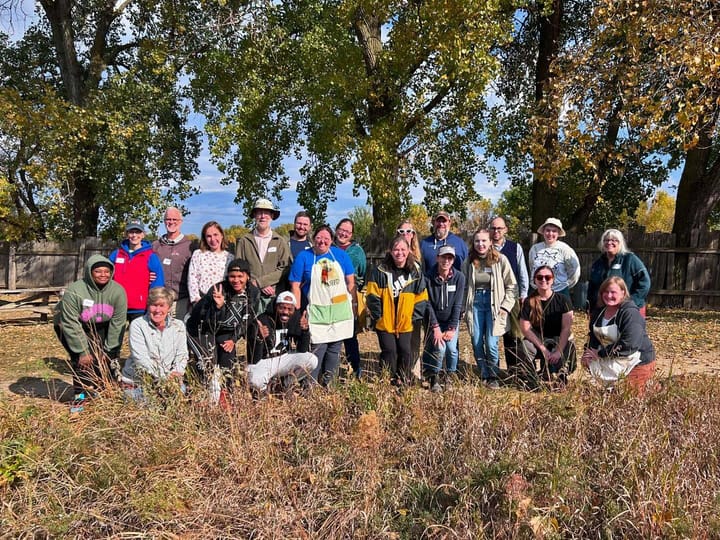 A group of people posing outdoors, surrounded by grasses and trees